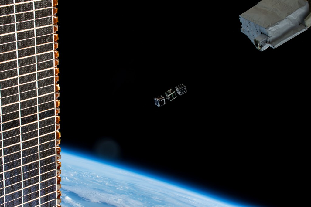 A trio of CubeSats (TUMnanoSAT, FUTABA, and HSU-SAT1) designed for education and research programs are pictured moments after their deployment from a small satellite deployer (top right) positioned outiside the Kibo laboratory module. The International Space Station was orbiting 259 miles above the Atlantic Ocean at the time of this photograph. A portion of one of the station's main solar arrays is also pictured at left.