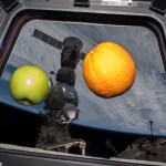 An apple and an orange are pictured floating weightlessly in the International Space Station's cupola. Seen outside the cupola, is the Soyuz MS-23 crew ship docked to the Prichal docking module which is attached to the Nauka science module.