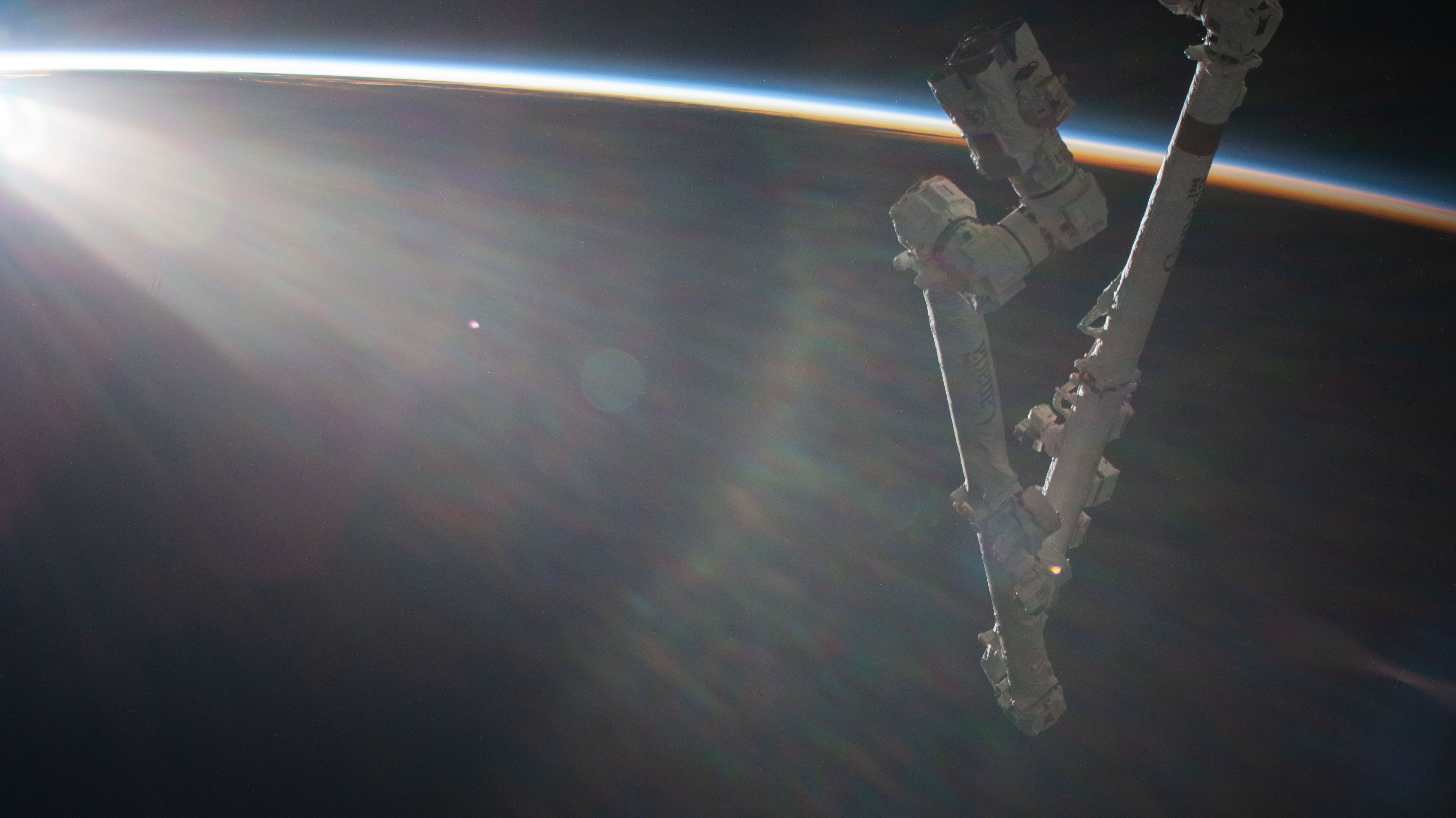An orbital sunrise begins illuminating Earth's atmosphere with the International Space Station's Canadarm2 robotic arm extending from the orbital lab as it soared 260 miles above the Pacific Ocean.