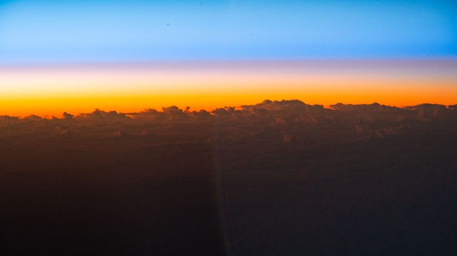 An orbital sunrise begins to illuminate the cloud tops in this photograph from the International Space Station as it orbited 258 miles above the Pacific Ocean south of the Hawaiian island chain.