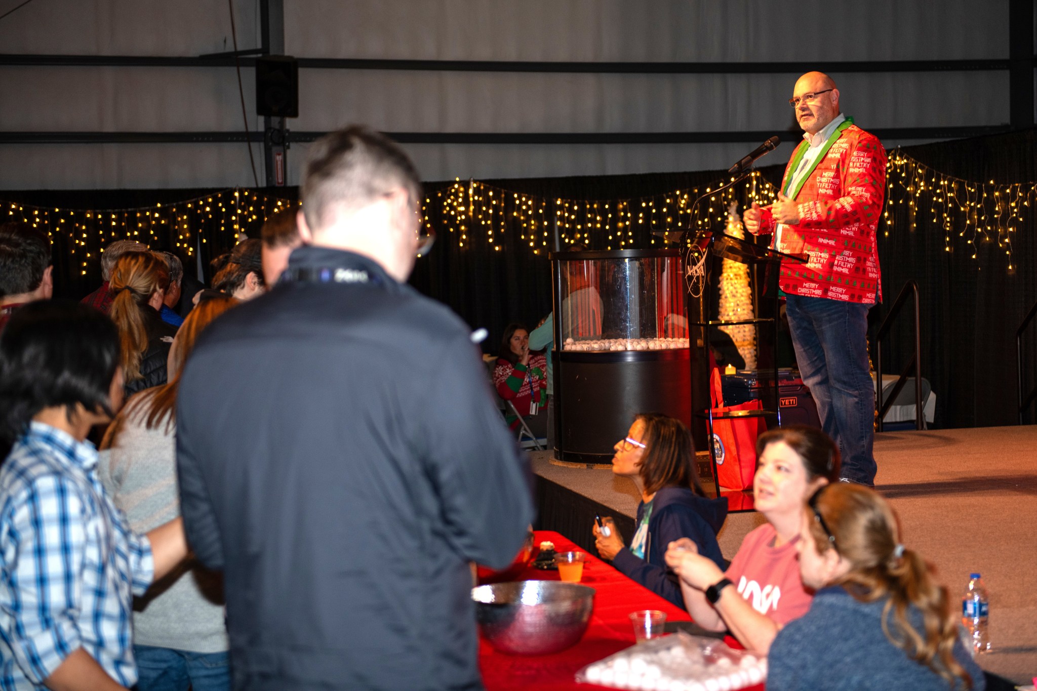 Marshall team members sign up for door prizes while Marshall Acting Center Director Joseph Pelfrey offers welcoming remarks at the center’s holiday reception.