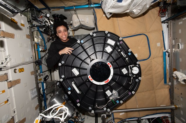 Expedition 67 Flight Engineer and NASA astronaut Jessica Watkins poses with the hatch cover belonging to the Bigelow Expandable Activity Module (BEAM) attached to the International Space Station's Tranquility module.