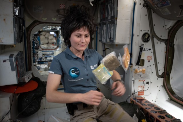 Expedition 67 Flight Engineer and ESA astronaut (European Space Agency) Samantha Cristoforetti poses with food packets flying weightlessly inside the International Space Station's Unity module.