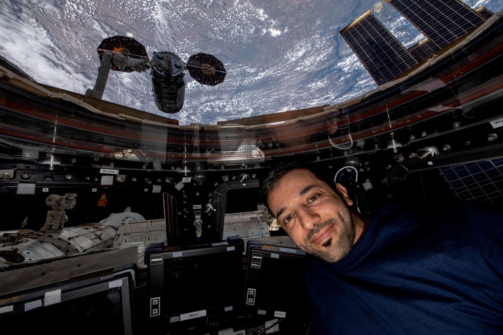 UAE (United Arab Emirates) astronaut and Expedition 69 Flight Engineer Sultan Alneyadi is pictured in the International Space Station's cupola with Northrop Grumman's Cygnus cargo craft outside in the grips of the Canadarm2 robotic arm.