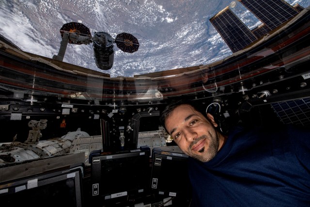 UAE (United Arab Emirates) astronaut and Expedition 69 Flight Engineer Sultan Alneyadi is pictured in the International Space Station's cupola with Northrop Grumman's Cygnus cargo craft outside in the grips of the Canadarm2 robotic arm.