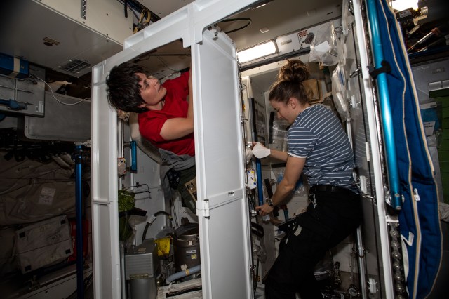 Expedition 67 Flight Engineers (from left) Samantha Cristoforetti of ESA (European Space Agency) and Kayla Barron of NASA partner together on orbital plumbing duties inside the two bathrooms aboard the International Space Station's Tranquility module.