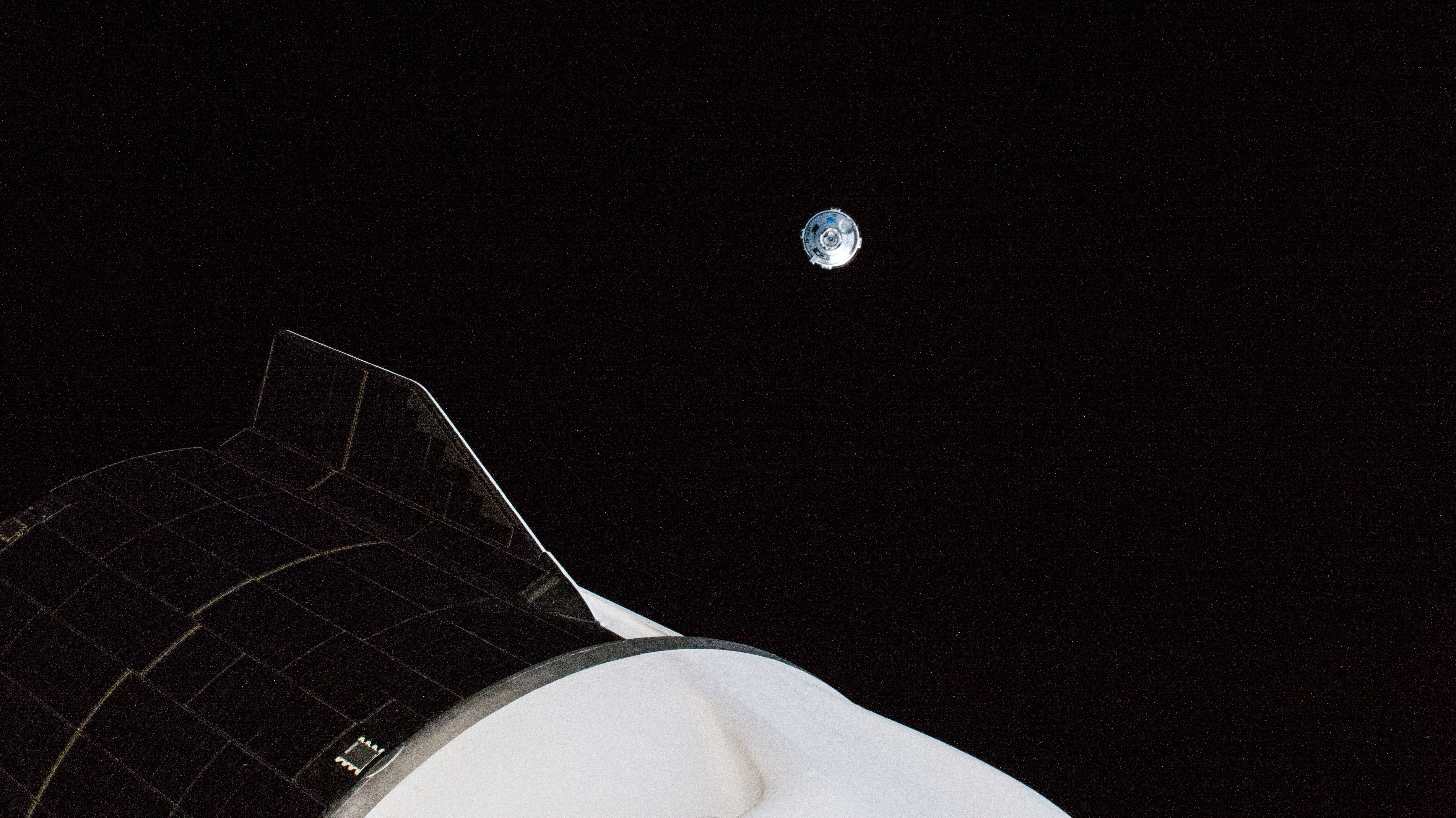 Boeing's CST-100 Starliner crew ship is pictured maneuvering away from the International Space Station after undocking from the Harmony module's forward port. In the foreground, is the aft end of the SpaceX Dragon Freedom crew ship that delivered the Crew-4 astronauts to the orbiting lab.