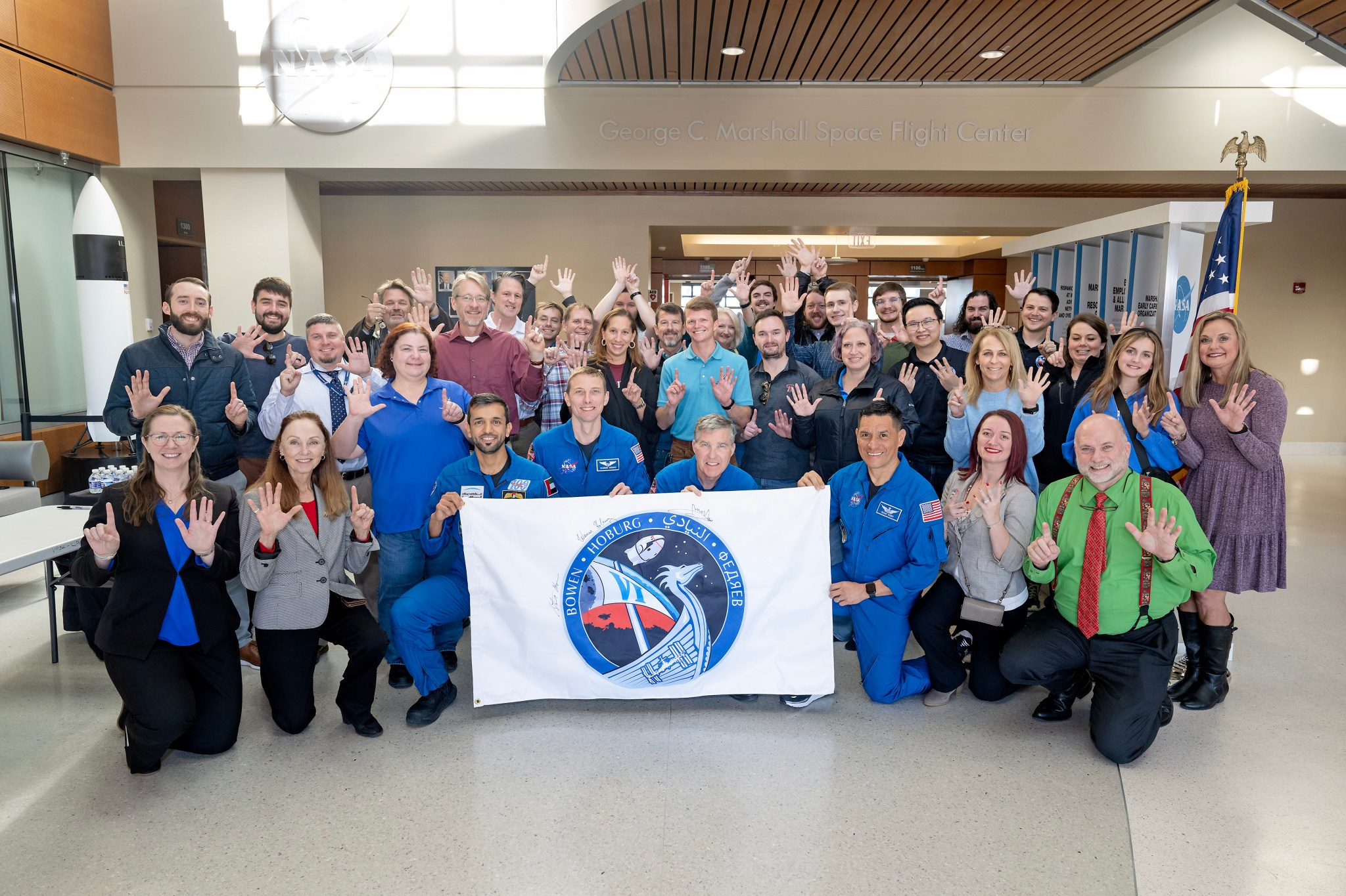 Expedition 69 Crew-6 astronauts smile and hold a banner for a photo with team members from the Human Exploration Development & Operations Office at NASA’s Marshall Space Flight Center. From left, the astronauts are Sultan Alneyadi, Steven Bowen, Warren “Woody” Hoburg, and Frank Rubio.
