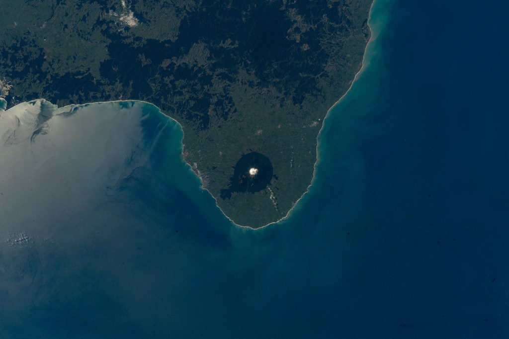 Egmont National Park, nearing the west coast of the North Island of New Zealand, is pictured as the International Space Station orbited roughly 270 miles above. The snow-capped stratovolcano, Mount Taranaki, sits at roughly 8,300 feet (~ 2,500 meters), surrounded by lush forests that provide strong visibility from low-Earth orbit.