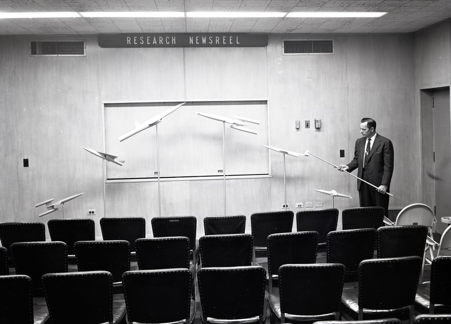 Man standing with chart in front of empty seats.