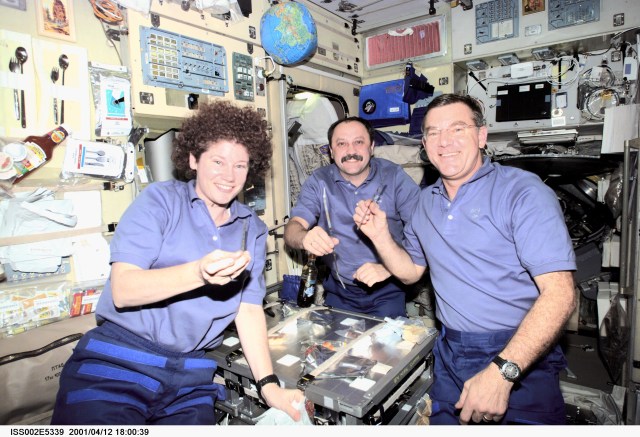 The Expedition Two crewmembers -- astronaut Susan J. Helms (left), cosmonaut Yury V. Usachev and astronaut James S. Voss -- share a meal at the table in the Zvezda Service Module of the International Space Station (ISS). This image was recorded with a digital still camera.