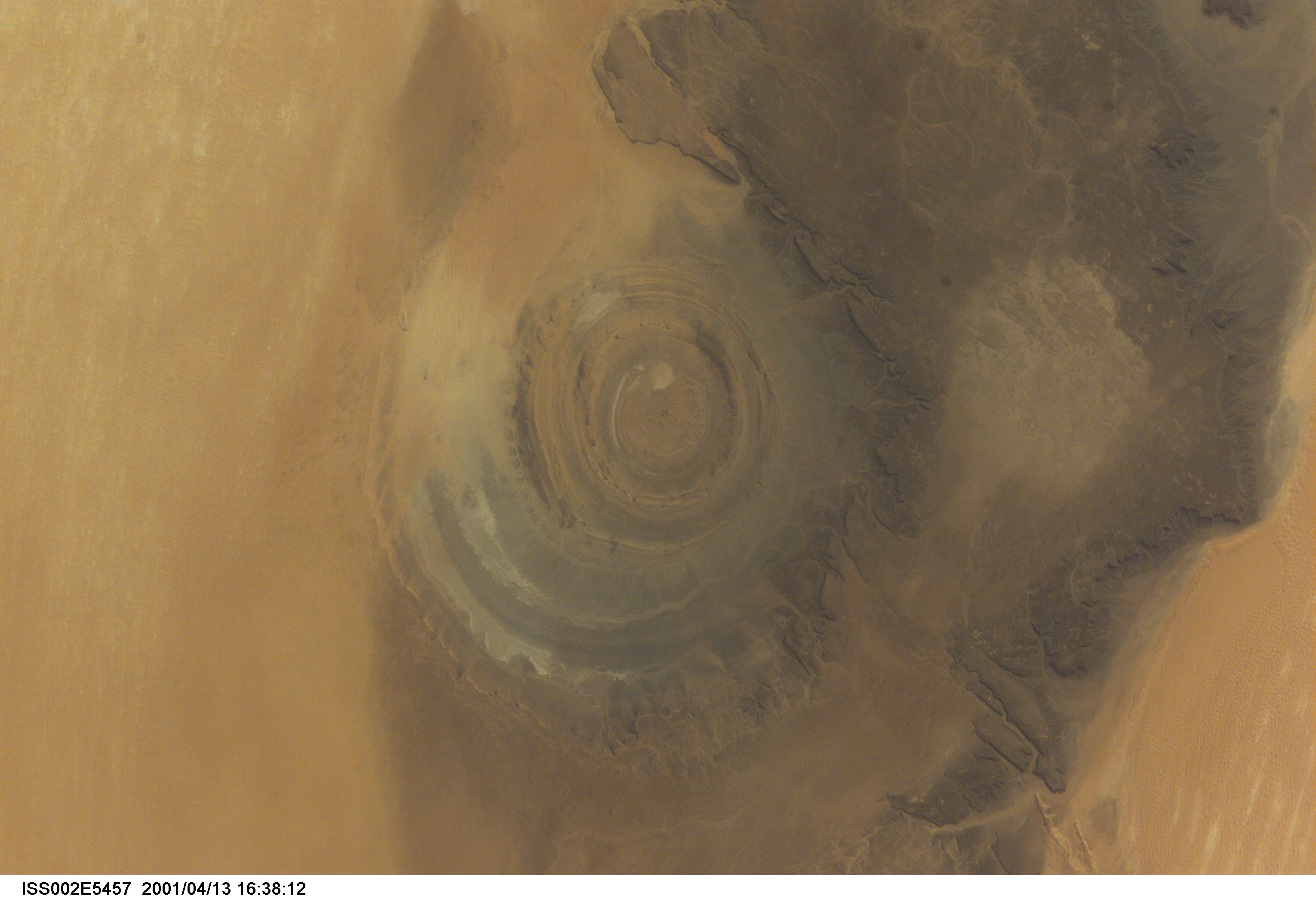 The "bull's-eye" of the Richat Structure adds interest to the barren Gres de Chinguetti Plateau in central Mauritania in northwest Africa. It represents domally uplifted, layered (sedimentary) rocks that have been eroded by water and wind into the present shape. The 25-mile-wide structure is a 300-foot-deep landmark that has caught the eye of many an astronaut in Earth orbit. Image number ISS002-E-5693 shows the same feature six days later. The image was recorded with a digital still camera.