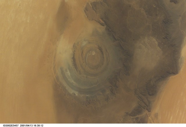 The "bull's-eye" of the Richat Structure adds interest to the barren Gres de Chinguetti Plateau in central Mauritania in northwest Africa. It represents domally uplifted, layered (sedimentary) rocks that have been eroded by water and wind into the present shape. The 25-mile-wide structure is a 300-foot-deep landmark that has caught the eye of many an astronaut in Earth orbit. Image number ISS002-E-5693 shows the same feature six days later. The image was recorded with a digital still camera.