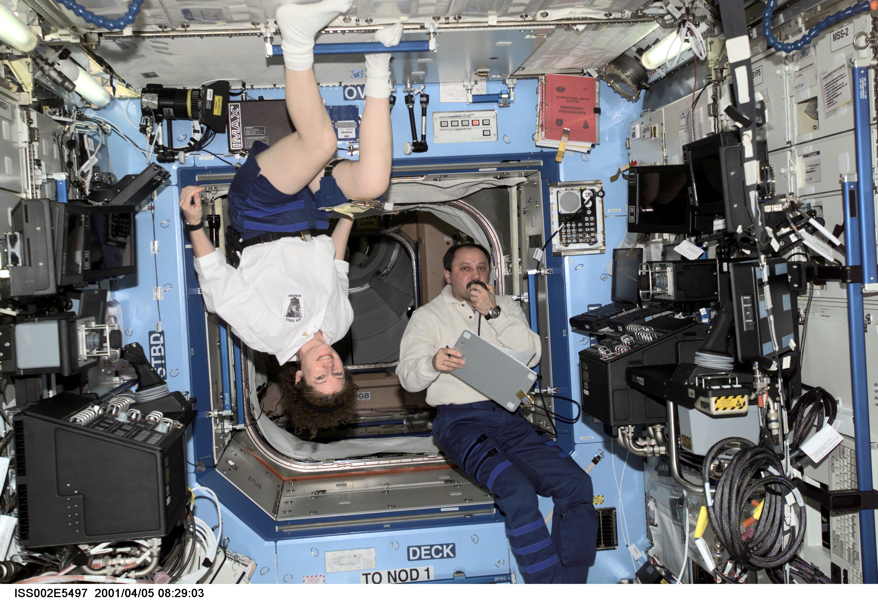 Astronaut Susan J. Helms (left), Expedition Two flight engineer, pauses from her work to pose for a photograph while Expedition Two mission commander, cosmonaut Yury V. Usachev, speaks into a microphone aboard the U.S. Laboratory / Destiny module of the International Space Station (ISS). This image was recorded with a digital still camera.