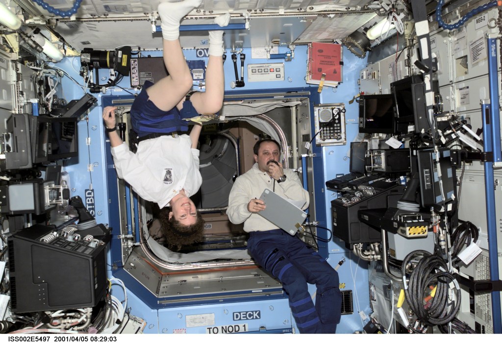 Astronaut Susan J. Helms (left), Expedition Two flight engineer, pauses from her work to pose for a photograph while Expedition Two mission commander, cosmonaut Yury V. Usachev, speaks into a microphone aboard the U.S. Laboratory / Destiny module of the International Space Station (ISS). This image was recorded with a digital still camera.
