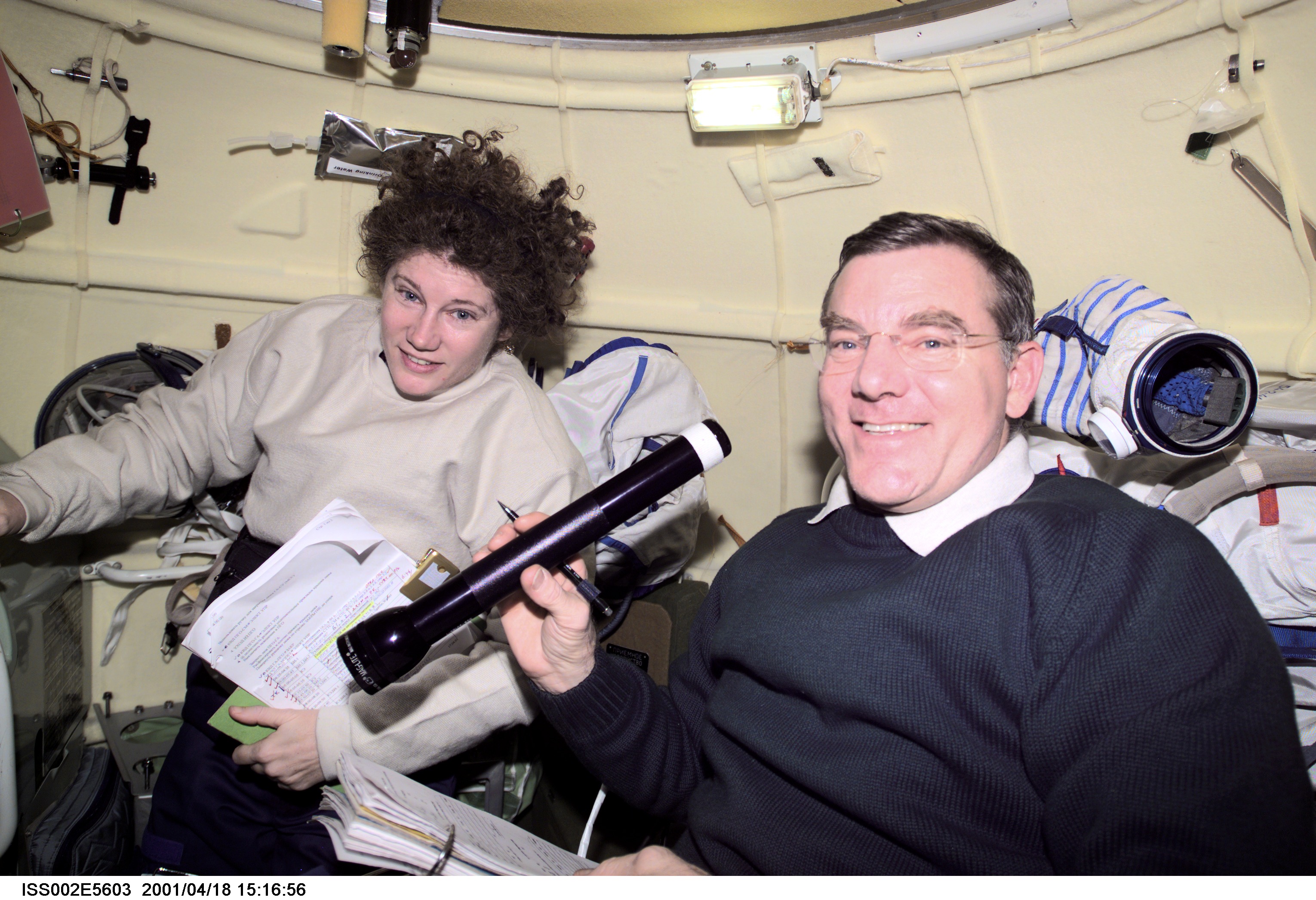 Astronauts Susan J. Helms and James S. Voss, both Expedition Two flight engineers, share a task in the Soyuz spacecraft which is docked to the International Space Station (ISS). The image was recorded with a digital still camera.