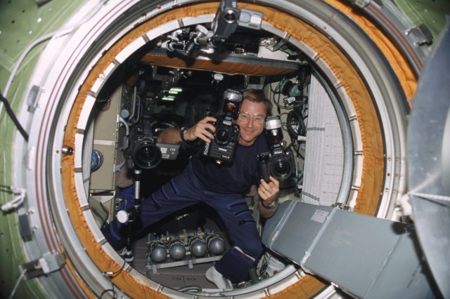 Astronaut Frank L. Culbertson, Jr., Expedition Three mission commander, carries cameras through the functional cargo block (FGB), or Zarya, hatch on the International Space Station (ISS).