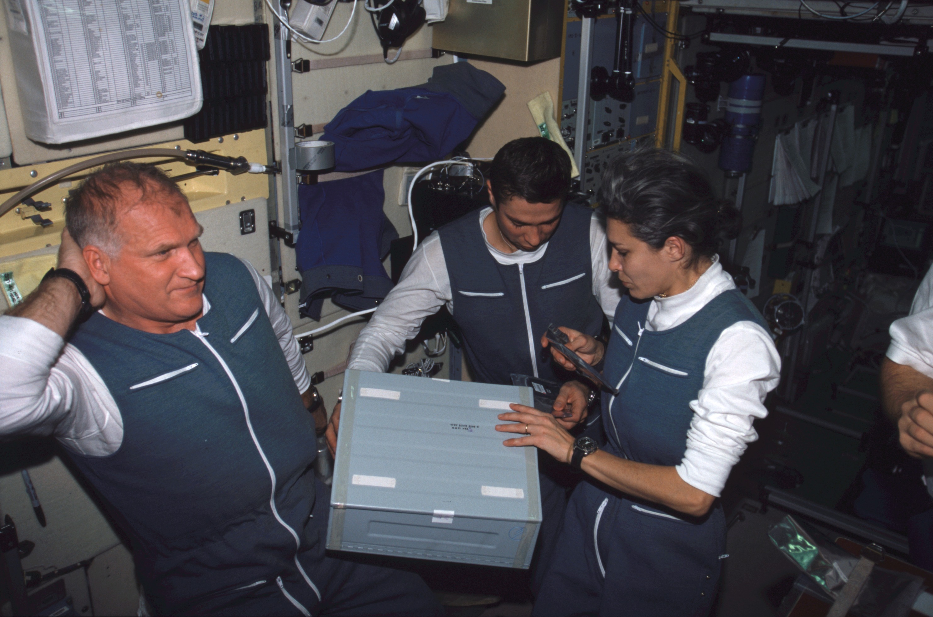 The Soyuz Taxi crew members go through a container in the Zvezda Service Module on the International Space Station (ISS). From the left are Commander Victor Afanasyev, Flight Engineer Konstantin Kozeev, and French Flight Engineer Claudie Haignere. Afanasyev and Kozeev represent Rosaviakosmos, and Haignere represents ESA, carrying out a flight program for CNES, the French Space Agency, under a commercial contract with the Rosaviakosmos.