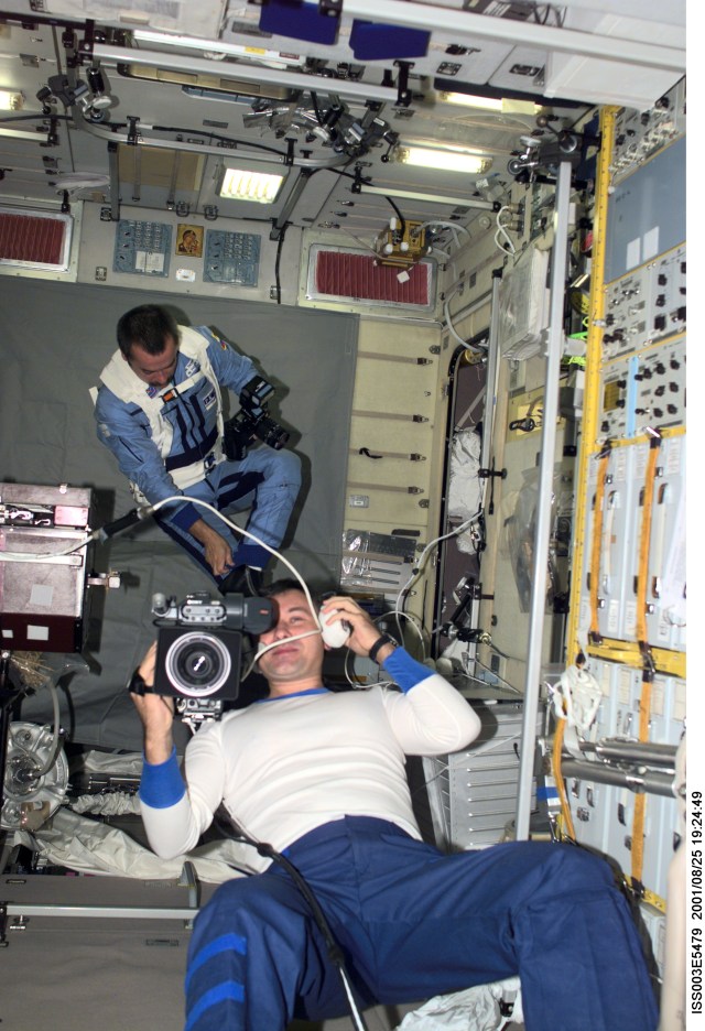 Cosmonaut Vladimir Dezhurov, Expedition Three flight engineer, operates a video camera in the Zvezda Service Module. In the background, cosmonaut Mikhail Tyurin, flight engineer, is visible with a photographic camera. Tyurin and Dezhurov represent Rosaviakosmos.