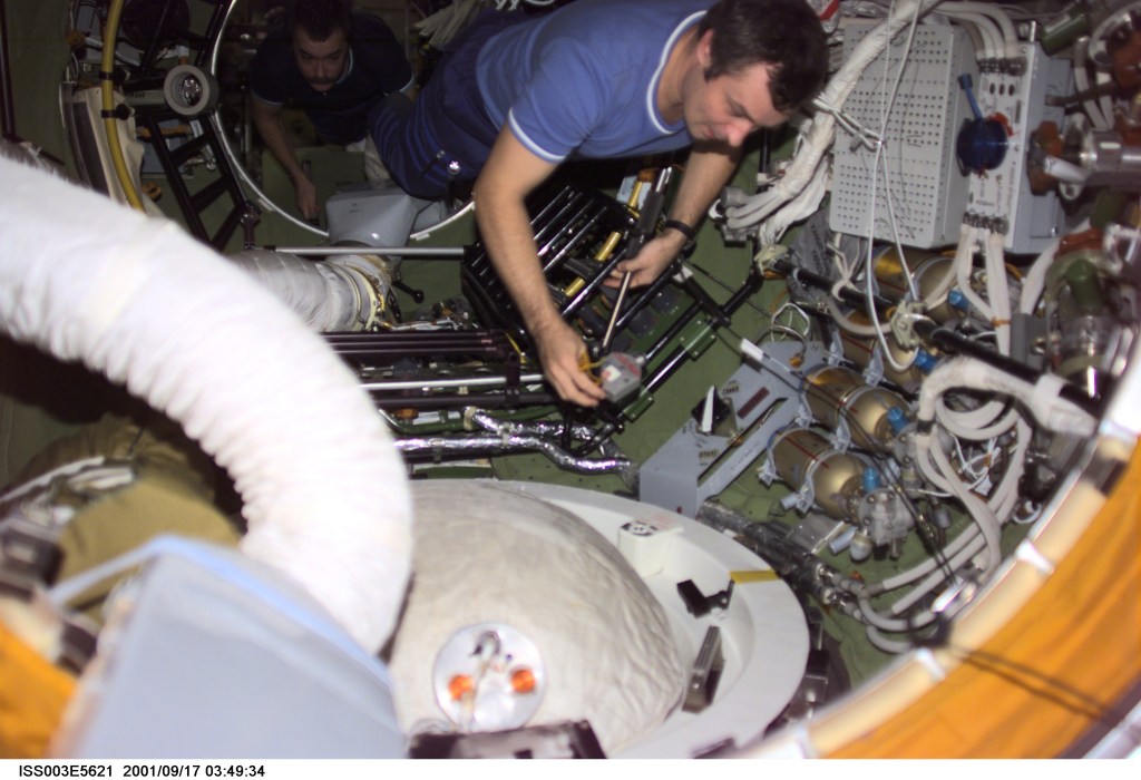 Cosmonaut Vladimir Dezhurov, Expedition Three flight engineer, prepares to remove the docking probe in the Zvezda Service Module's pressurized adapter. The docking probe successfully guided the arrival of the Russian-built Pirs docking compartment to the International Space Station (ISS). Mikhail Tyurin, flight engineer, is visible in the background. Tyurin and Dezhurov represent Rosaviakosmos.