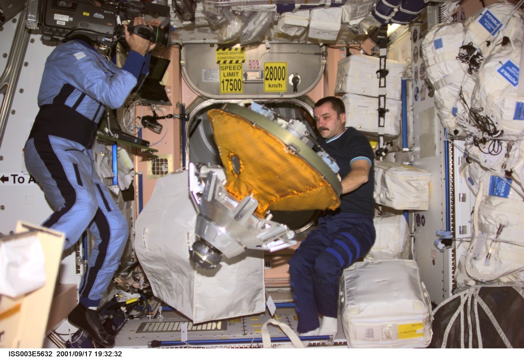 Cosmonaut Mikhail Tyurin, Expedition Three flight engineer, packs the docking probe in a stowage bag in Unity. Cosmonaut Vladimir Dezhurov, flight engineer, videotapes the event. The docking probe successfully guided the arrival of the Russian-built Pirs docking compartment to the International Space Station (ISS). Tyurin and Dezhurov represent Rosaviakosmos.