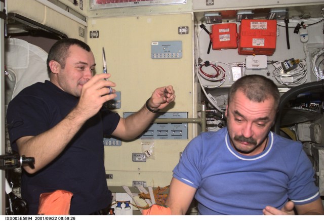 Cosmonauts Vladimir N. Dezhurov (left) and Mikhail Tyurin, Expedition Three flight engineers representing Rosaviakosmos, take turns cutting hair in the Zvezda Service Module on the International Space Station (ISS). This image was taken with a digital still camera.