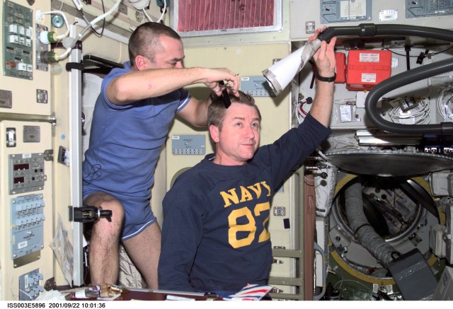 Astronaut Frank L. Culbertson, Jr. (right), Expedition Three mission commander, holds a vacuum device the crew has fashioned to garner freshly cut hair floating freely, as Mikhail Tyurin cuts his hair in the Zvezda Service Module on the International Space Station (ISS). Tyurin is a flight engineer representing Rosaviakosmos. This image was taken with a digital still camera.