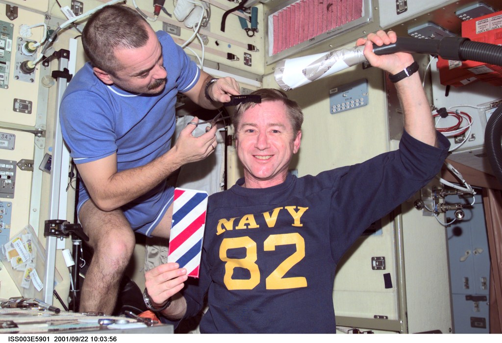 Astronaut Frank L. Culbertson, Jr. (right), Expedition Three mission commander, holds a vacuum device the crew has fashioned to garner freshly cut hair floating freely, as Mikhail Tyurin cuts his hair in the Zvezda Service Module on the International Space Station (ISS). Tyurin is a flight engineer representing Rosaviakosmos. This image was taken with a digital still camera.