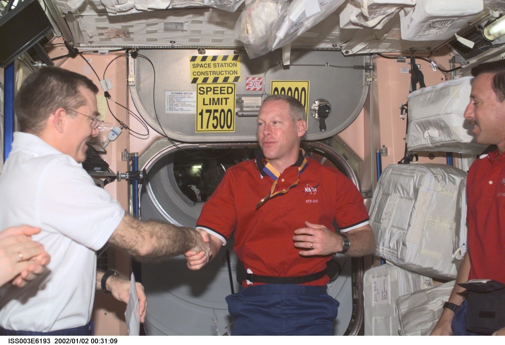 Astronauts James S. Voss (left), Expedition Two flight engineer, Patrick G. Forrester, STS-105 mission specialist, and Scott J. Horowitz, mission commander, exchange greetings in the Unity node on the International Space Station (ISS). This image was taken with a digital still camera.