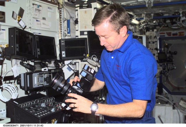 Astronaut Frank L. Culbertson, Jr., Expedition Three mission commander, works with a digital still camera (DSC) in the Destiny laboratory on the International Space Station (ISS). Controls for the Canadarm2 are visible to the right of Culbertson. This image was taken with a DSC.