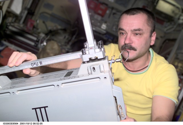 Cosmonaut Mikhail Tyurin, Expedition Three flight engineer representing Rosaviakosmos, works with Japan’s National Space Development Agency (NASDA) hardware for the Micro-Particles Capturer (MPAC) and Space Environment Exposure Device (SEED) experiment in the Zvezda Service Module on the International Space Station (ISS). This image was taken with a digital still camera.