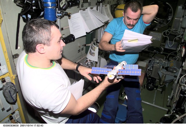 Cosmonaut Vladimir N. Dezhurov (foreground) holds a model of the International Space Station (ISS) as cosmonaut Mikhail Tyurin reads a procedures checklist in the Zvezda Service Module on the ISS. Dezhurov and Tyurin are both Expedition Three flight engineers representing Rosaviakosmos. This image was taken with a digital still camera.