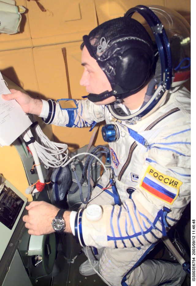 Cosmonaut Vladimir N. Dezhurov, Expedition Three flight engineer, wearing a Russian Sokol suit, checks a procedures checklist in the Soyuz spacecraft that is docked to the International Space Station (ISS). This Soyuz return vehicle will be moved from the Earth-facing port of the Zarya module for the linkup to the new Pirs Docking Compartment. The move of the Soyuz will mark the first time the new Pirs, which arrived at the station September 17, 2001, will serve as a docking port. The Soyuz will be shifted to prepare for the arrival of a new Soyuz return craft, to be launched October 21, 2001 from the Baikonur Cosmodrome in Kazakhstan. The Soyuz can serve as a crew return vehicle at the station for a maximum of about six months. Dezhurov represents Rosaviakosmos. This image was taken with a digital still camera.