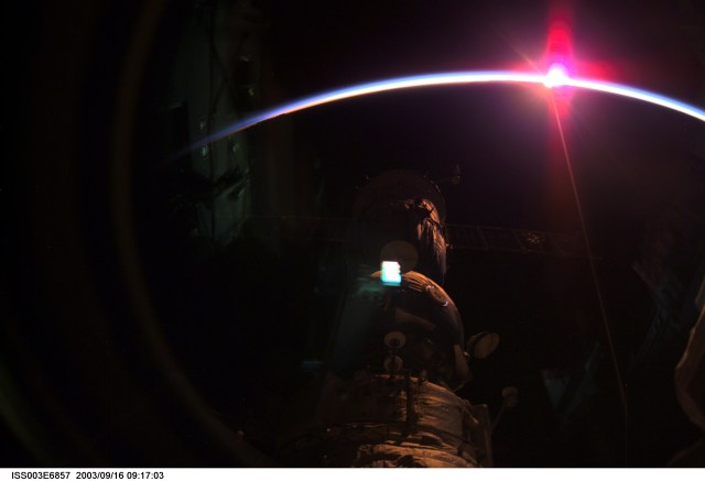 Using a digital still camera, the International Space Station (ISS) Expedition Three crew members captured a setting sun and the thin blue airglow line at Earth's horizon. Some of the station's components are silhouetted in the foreground.