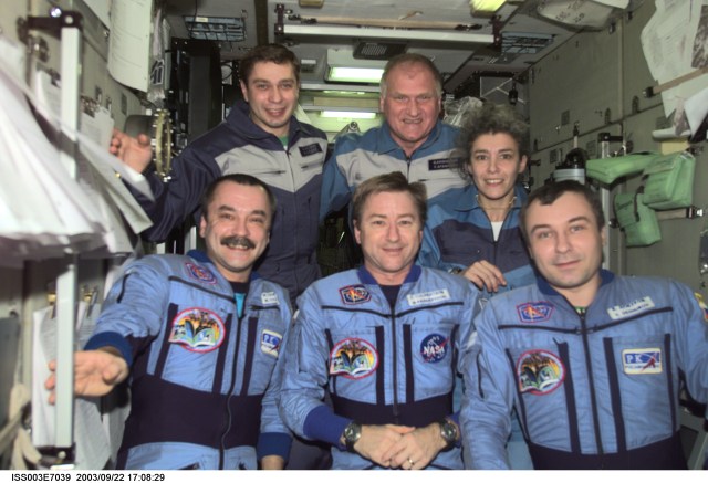 The Expedition Three crew (bottom) and the Soyuz Taxi crew assemble for a group photo in the Zvezda Service Module on the International Space Station (ISS). The Expedition Three crewmembers are astronaut Frank L. Culbertson, Jr. (center), mission commander, and cosmonauts Mikhail Tyurin (left) and Vladimir N. Dezhurov, both flight engineers. The Soyuz taxi crewmembers are Flight Engineer Konstantin Kozeev (left), Commander Victor Afanasyev, and French Flight Engineer Claudie Haignere. Tyurin, Dezhurov, Afanasyev, and Kozeev represent Rosaviakosmos. Haignere represents ESA, carrying out a flight program for CNES, the French Space Agency, under a commercial contract with the Russian Aviation and Space Agency. This image was taken with a digital still camera.