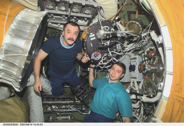 Cosmonaut Mikhail Tyurin (left), Expedition Three flight engineer, and Soyuz Taxi crewmember, Flight Engineer Konstantin Kozeev, work in the Zvezda Service Module’s transfer compartment on the International Space Station (ISS). Tyurin and Kozeev represent Rosaviakosmos.