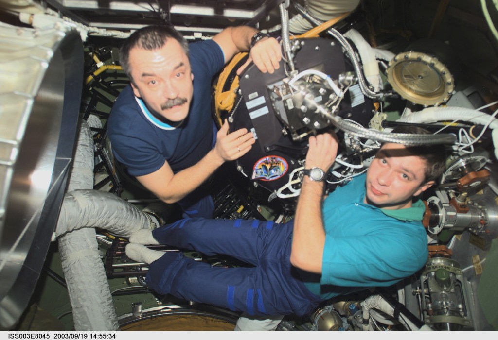 Cosmonaut Mikhail Tyurin (left), Expedition Three flight engineer, and Soyuz Taxi crewmember, Flight Engineer Konstantin Kozeev, work in the Zvezda Service Module’s transfer compartment on the International Space Station (ISS). Tyurin and Kozeev represent Rosaviakosmos.