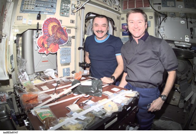 Cosmonaut Mikhail Tyurin (left), Expedition 3 flight engineer, and astronaut Frank L. Culbertson, mission commander, eat a Thanksgiving meal in the Zvezda Service Module on the International Space Station (ISS). Tyurin represents Rosaviakosmos.