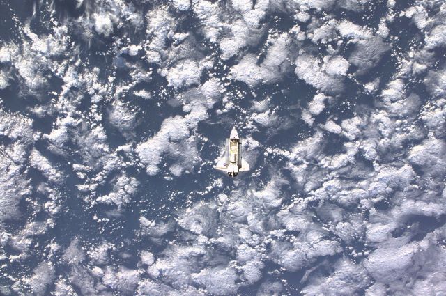 Space Shuttle Endeavour is almost lost in this distant image as the mostly white vehicle is backdropped against a large cloud mass on Earth. Controlled by the flight crew of STS-108, the shuttle was approaching the International Space Station (ISS), from which this digital image was recorded. Among other activities the Endeavour's mission will include the change out of the station crews.