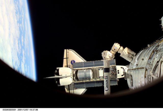 The Space Shuttle Endeavour, controlled by the flight crew of STS-108, is backdropped against the blackness of space over Earth's horizon as it approaches the International Space Station (ISS). The Raffaello logistics module that is being brought up to the orbiting outpost is clearly visible in Endeavour's cargo bay. The Space Station Remote Manipulator System (SSRMS) or Canadarm2 is visible at lower right. Among other activities the Endeavour's mission will include the change out of the station crews. The image was recorded with a digital still camera.