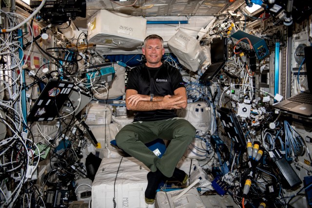 Mogensen floats in the center of the Columbus laboratory module. Several cables, boxes, and laptops are secured to the walls around him.