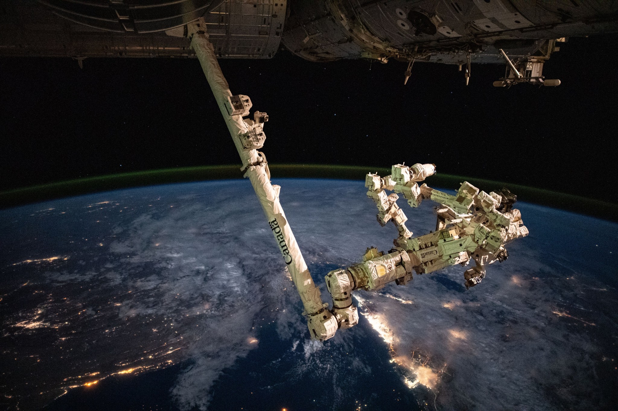 Esta imagen muestra el brazo robótico Canadarm2 extendiéndose por debajo de la Estación Espacial Internacional mientras esta orbita a 418 kilómetros (260 millas) de altura sobre las luces de las ciudades de la península arábiga.