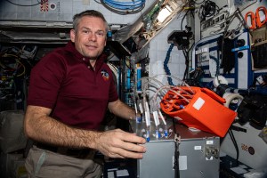 Andreas Mogenson looks at the camera while working on an orange box with several tubes sticking out of it floating next to him.