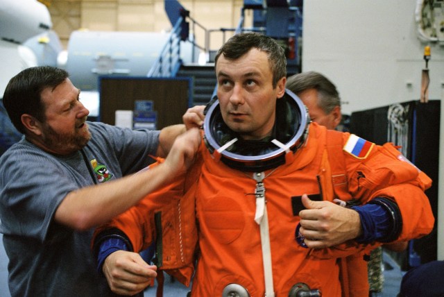 Cosmonaut Vladimir N. Dezhurov, Expedition Three flight engineer, is assisted in his suiting process by United Space Alliance (USA) suit technicians Steve Clendenin (left) and Jim Cheatham (partially obscured), during mission training at the Johnson Space Center’s System Integration Facility. Dezhurov is affiliated with Rosaviakosmos. The suit is a training version of the full pressure garment crew members wear for ascent and entry.