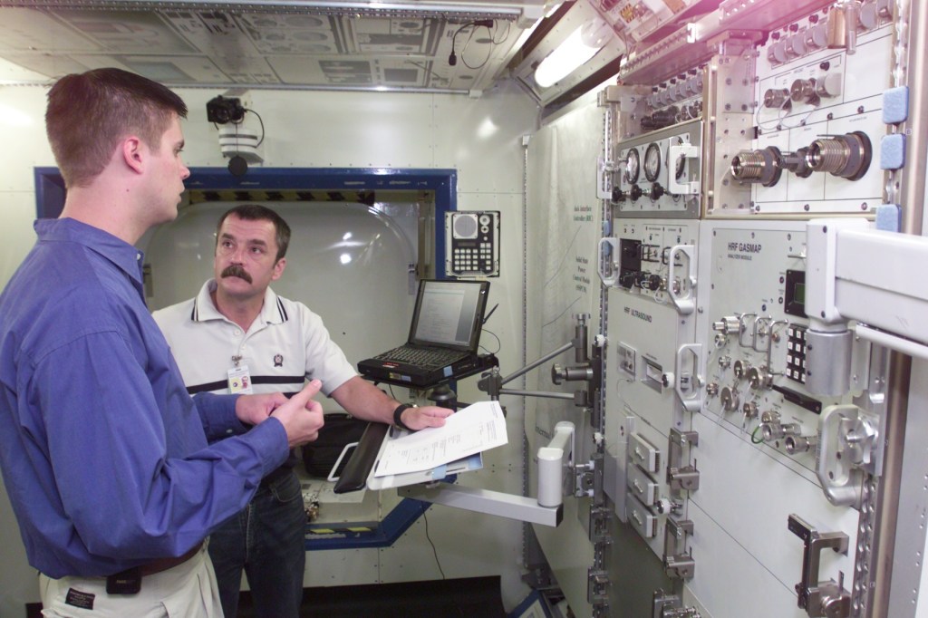 Cosmonaut Mikhail Tyurin, Expedition Three flight engineer representing Rosaviakosmos, is photographed in Human Research Facility (HRF) Rack training in the International Space Station (ISS) Destiny laboratory mockup/trainer at the Johnson Space Center’s Systems Integration Facility. The cosmonaut is being assisted by trainer Christian Maender.