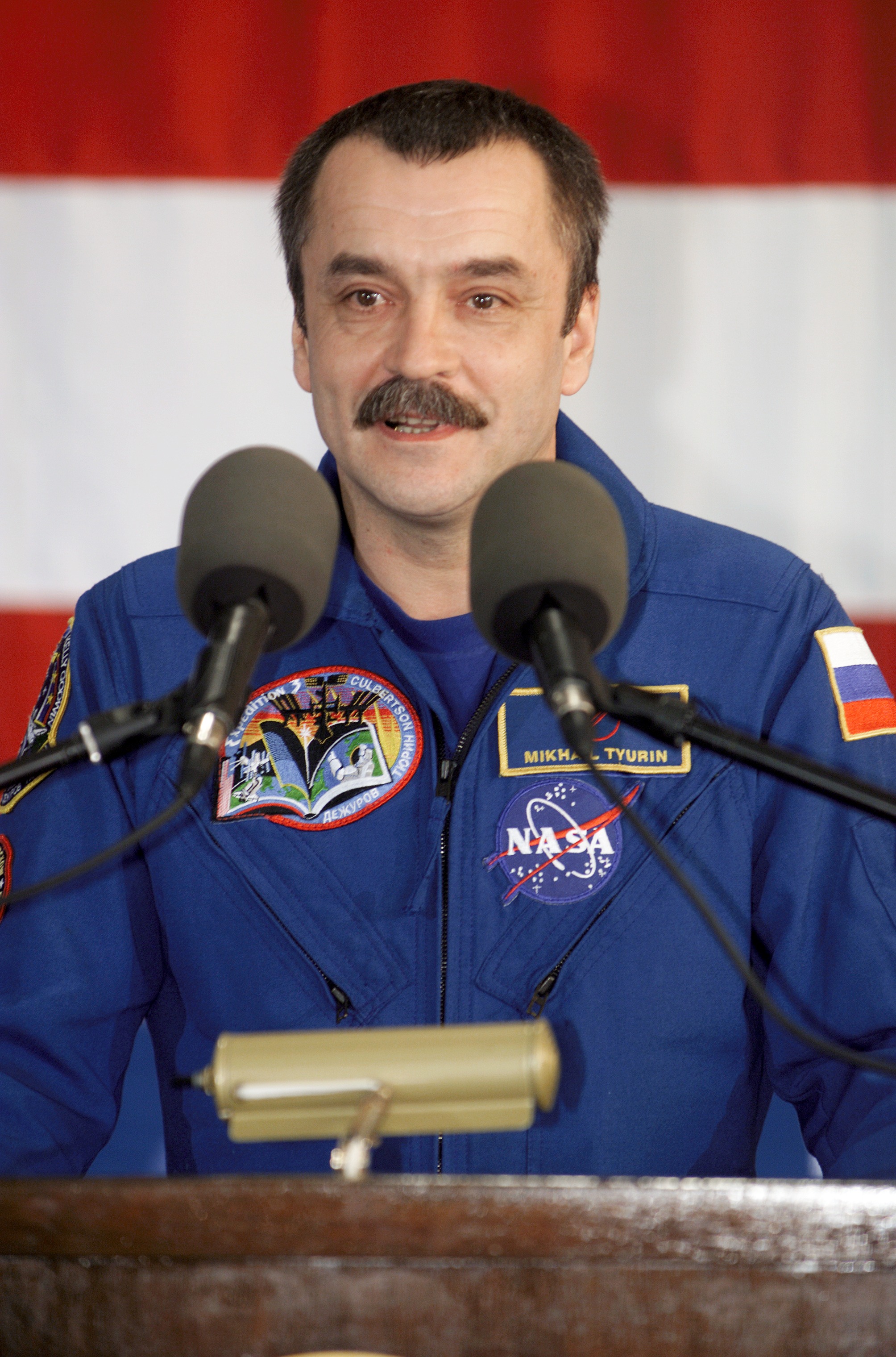 Cosmonaut Mikhail Tyurin, Expedition Three flight engineer representing Rosaviakosmos, speaks from the podium in Hangar 990 at Ellington Field during the STS-108 and Expedition Three crew return ceremonies. The STS-108 crew delivered the Expedition Four crew and supplies to the International Space Station (ISS) and brought the Expedition Three crew back to Earth.