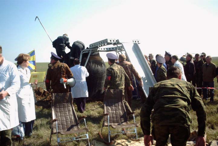 Aid and rescue team members communicate with Soyuz 4 taxi crewmembers inside the Soyuz TM-33 spacecraft while others stand ready with a special device called the crew extraction stand. The team later fit the device, which has both a ladder and a slide, to the Soyuz. The stand makes it possible for the crewmembers to egress the spacecraft without their feet touching the ground. Three chairs await the crewmembers in the foreground. Landing occurred around 7:52 a.m. Moscow time near Arkalyk, Kazakhstan. Having spent 10 days in space, the majority of that time onboard the International Space Station (ISS), still inside the spacecraft are Yuri Gidzenko, commander; Roberto Vittori, flight engineer; and space flight participant Mark Shuttleworth of South Africa. Gidzenko is with Rosaviakosmos and Vittori represents the European Space Agency (ESA). Photo Credit: NASA/Marty Linde