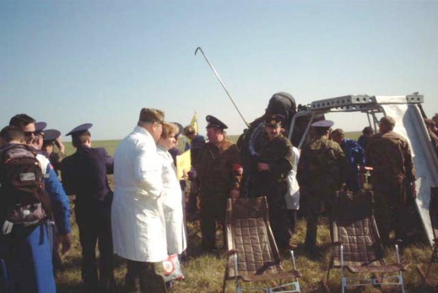 An aid and rescue team member stands atop the Soyuz TM-33 spacecraft (partially obscured by rescue equipment and team members in background), while others stand ready with a special device called the crew extraction stand. The team later fit the device, which has both a ladder and a slide, to the Soyuz. The stand makes it possible for the crewmembers to egress the spacecraft without their feet touching the ground. Three chairs await the crewmembers in the foreground. Landing occurred around 7:52 a.m. Moscow time. Having spent 10 days in space, the majority of that time onboard the International Space Station (ISS), and still inside the spacecraft are Yuri Gidzenko, commander; Roberto Vittori, flight engineer; and space flight participant Mark Shuttleworth of South Africa. Gidzenko is with Rosaviakosmos and Vittori represents the European Space Agency (ESA). Photo Credit: NASA/Marty Linde