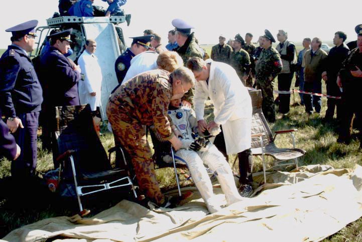 Aid and rescue team members ease Yuri Gidzenko, Soyuz 4 commander, into a chair following his egress from the Soyuz TM-33 spacecraft in the background. Ground crewmembers begin to assist the egress of Roberto Vittori (not visible), flight engineer. The Soyuz touched down at 7:52 a.m. (Moscow time) in a field near Arkalyk, Kazakhstan. Photo Credit: NASA/Marty Linde
