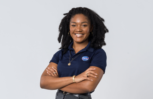 Smiling young black woman in a NASA shirt folds her arms.